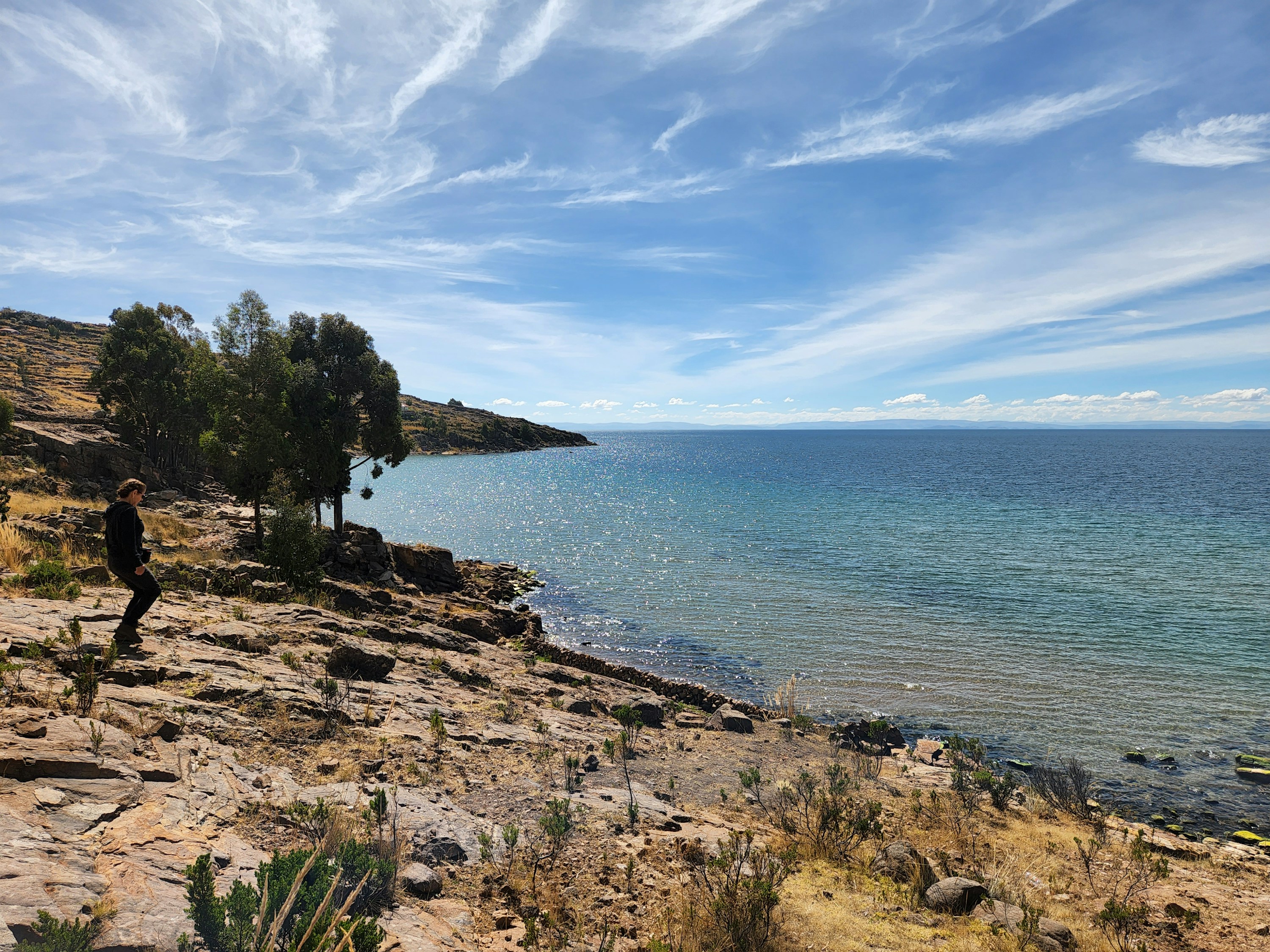 A traveler walking along the rocky shore of Taquile Island above Lake Titicaca