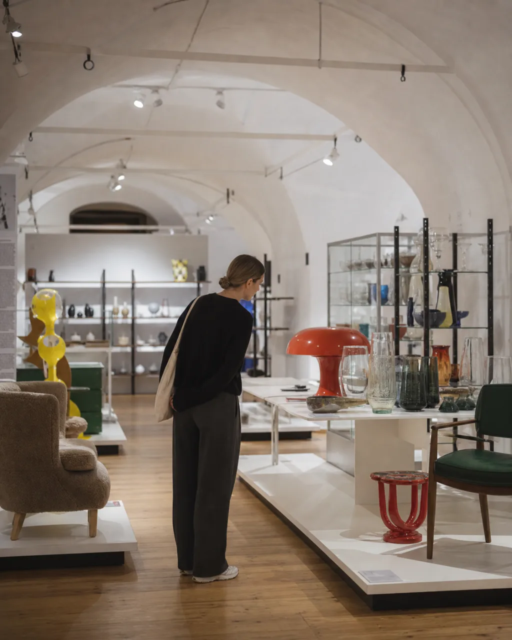Visitor comparing Estonian glass, furniture and lighting in ETDM's vaulted gallery