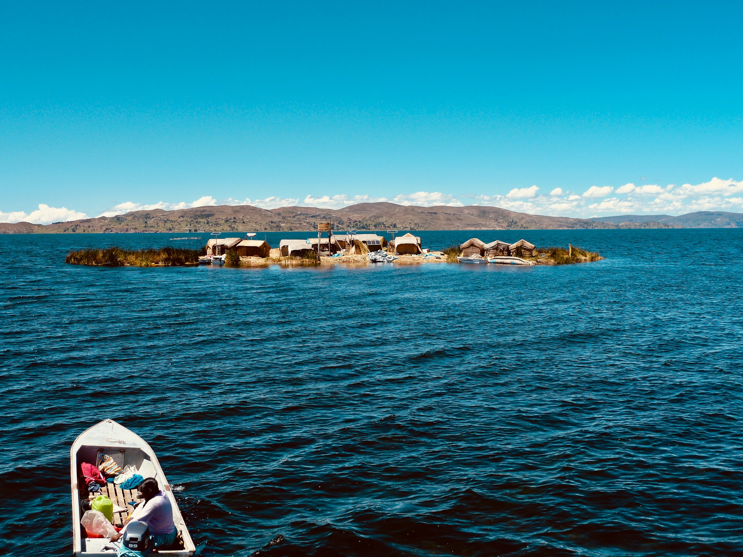 A small boat crossing blue Lake Titicaca toward the floating Uros islands
